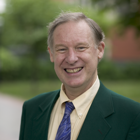 Professor White standing outside smiling in a green blazer and purple tie