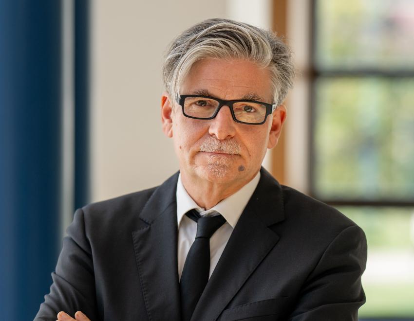 Professor Müller standing in bright room with arms crossed 