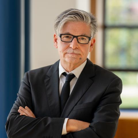 Professor Müller standing in bright room with arms crossed 